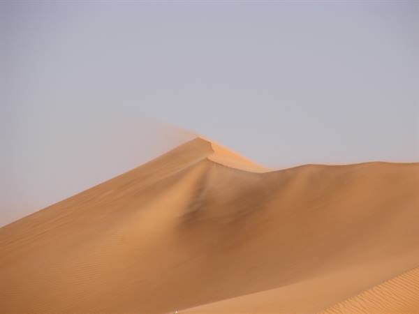 Wind-blown sand drifting off a desert dune crest