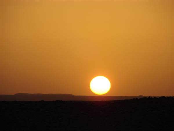 Low orange sun sinking over a dark desert horizon