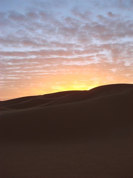 Dark sand dunes beneath an orange and blue cloudy sky