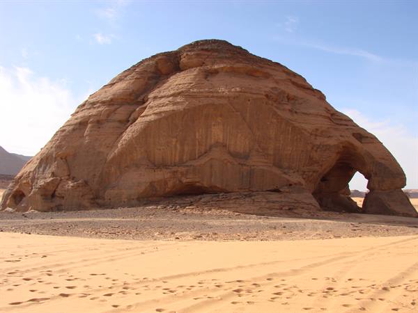 Sandstone monolith with natural arch in the sandy desert