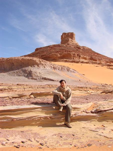 Woman sitting on sandstone rock in the desert, rocky outcrop behind