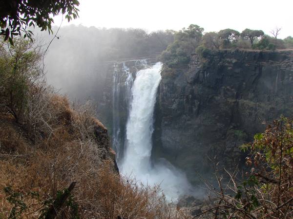 Powerful waterfall plunging into rocky gorge, mist rising, dry bushes, Victoria Falls