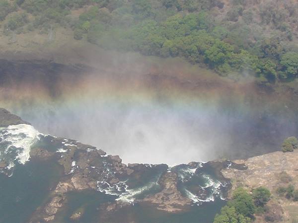 Rainbow over the spray of Victoria Falls, Zambezi river among rocks