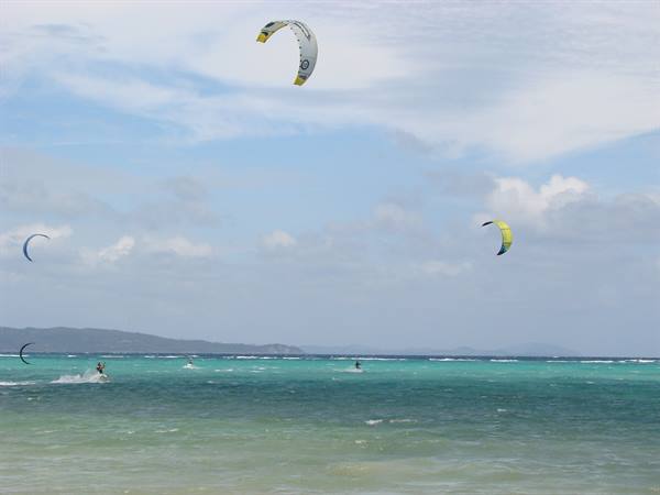 Kitesurfers with yellow and white kites glide across turquoise sea under clouds