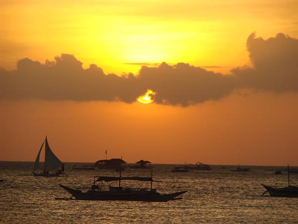 Sailboats silhouetted on the golden sea, sun filtering through the clouds