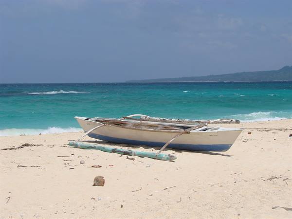 White and blue outrigger fishing boat stranded on the sandy beach