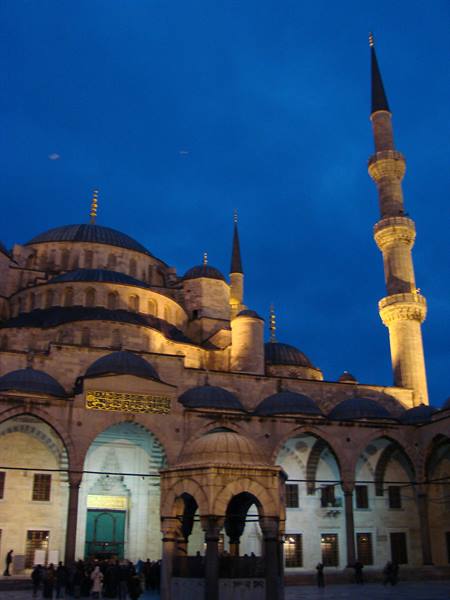 Istanbul's Blue Mosque lit at night with minaret and visitors in the courtyard