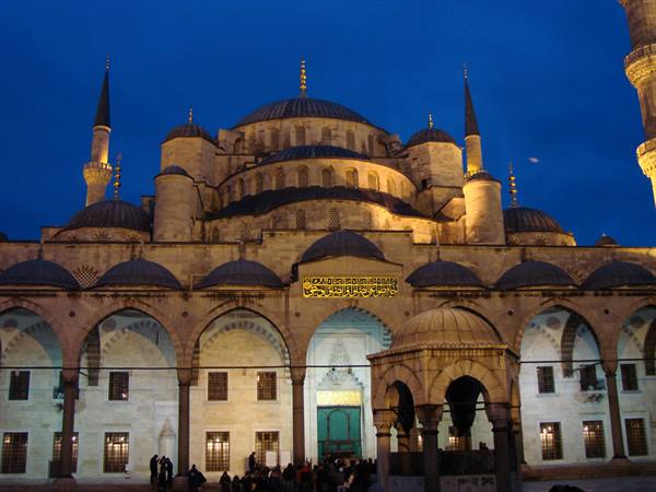 Blue Mosque in Istanbul illuminated at dusk, Visitors in the courtyard with fountain