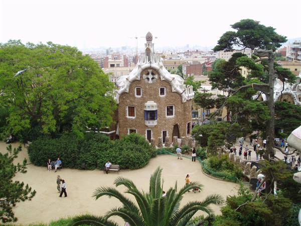 Stone house with undulating roof at Park Güell, visitors among pines and palms