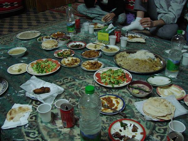 Rice platter, salads and flatbread on a carpet, people sitting sharing the meal