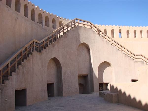 Wooden staircase over arched mud-brick fortress walls under blue sky