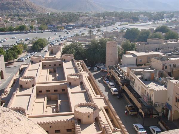 Mud-brick fort in Nizwa with crenellated towers above town and mountains