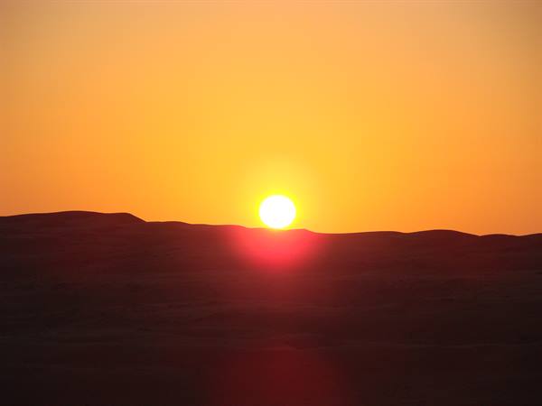 Sun rising over dark sand dunes, intense orange sky