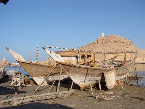 Wooden dhows under repair on shore supports at a shipyard, clear blue sky