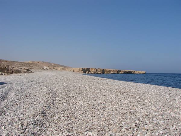 White pebble beach beneath limestone cliffs and blue sea