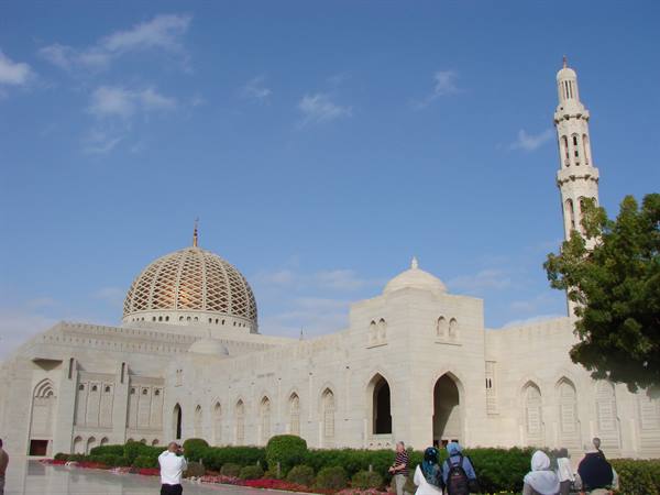Tourists photograph the Sultan Qaboos Grand Mosque, white marble and minaret under blue sky