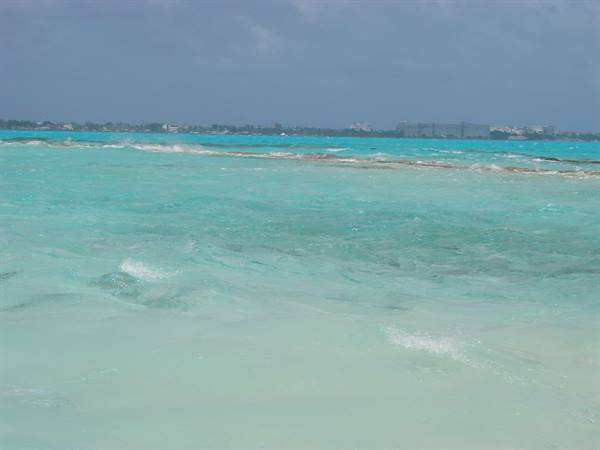 Turquoise water with foam, sandbar and distant coastline hotels under cloudy sky