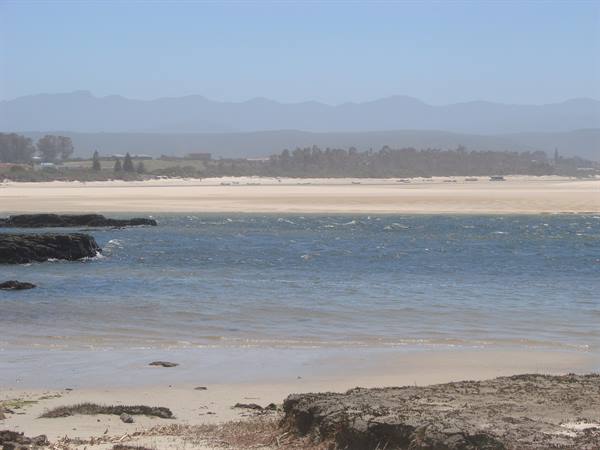 Waves on sand before a deserted beach, dark rocks and hazy mountains