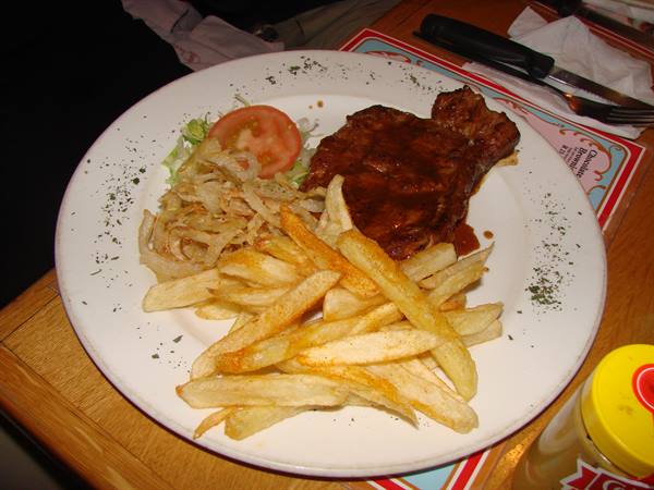 Steak with sauce, fries and onions on white plate at table