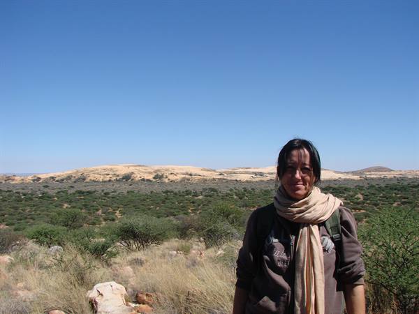 Woman with beige scarf and backpack in savanna, sandy hills under blue sky