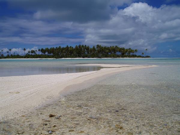 Clear lagoon with a strip of white sand and palm trees on the horizon