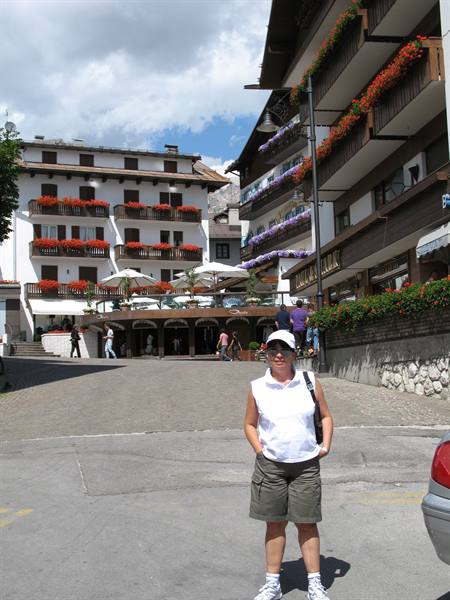 Smiling woman in Cortina d'Ampezzo town center, among flowered hotel balconies and umbrellas
