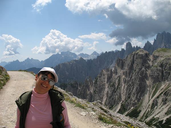 Smiling tourist in white cap on a trail among Dolomite peaks