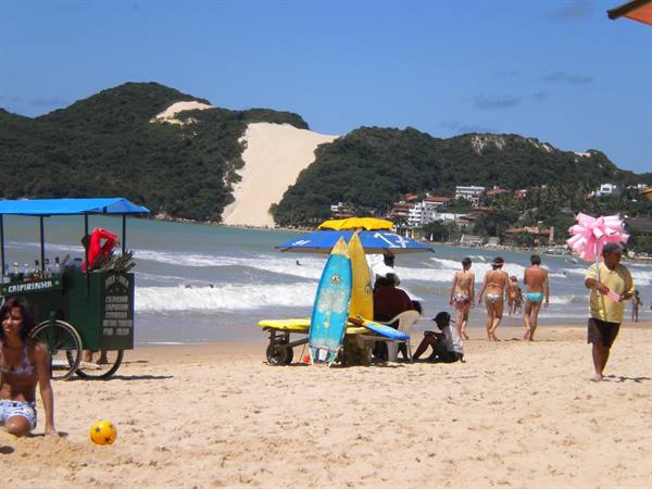 Beach with bathers, surfboards, caipirinha cart and green dune in background