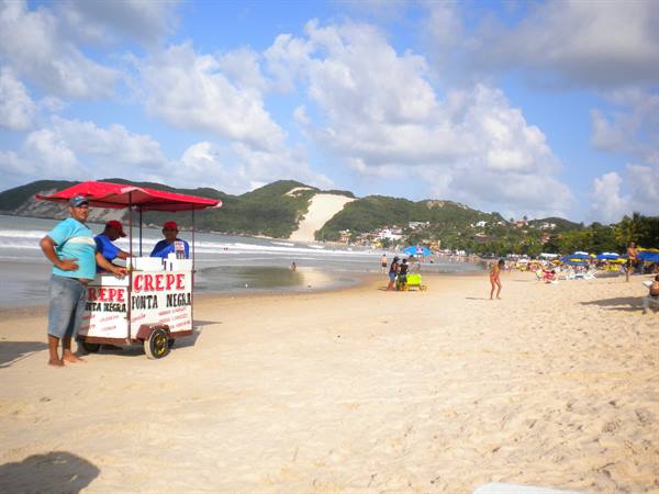 Crepe vendors with a cart on the sand, busy beach and green dune behind