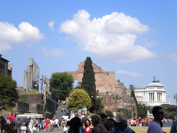 Tourists strolling along the Imperial Forums, Roman columns and Vittoriano monument under clouds