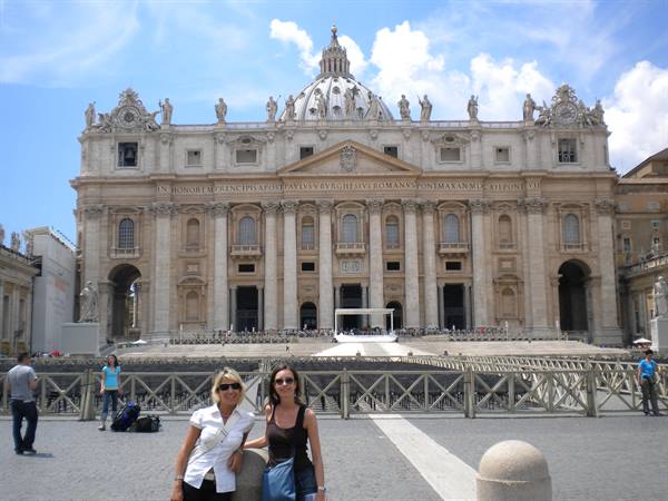 Two tourists in sunglasses pose in front of St. Peter's Basilica facade