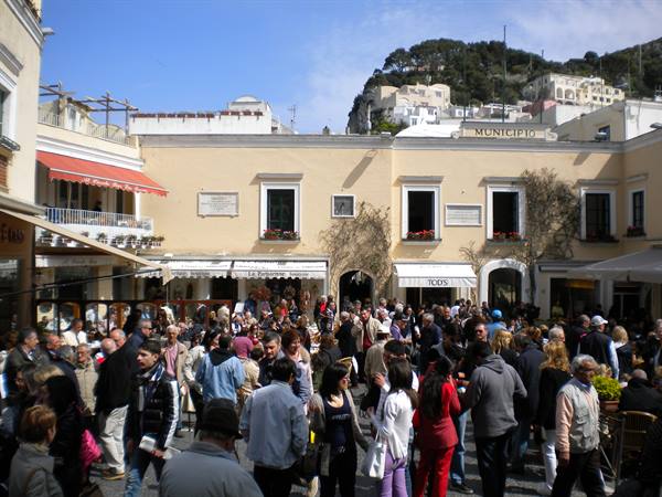 Crowd of tourists in the town square in Capri, yellow houses under sun