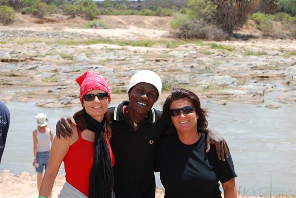 Three friends embrace and smile in front of a rocky river