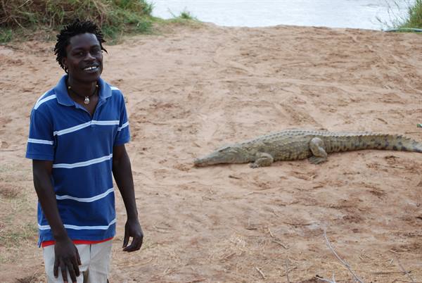 Smiling young man in striped polo shirt next to a crocodile on sand