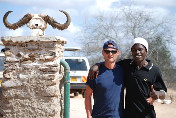Two smiling men beside a stone pillar topped with a buffalo skull