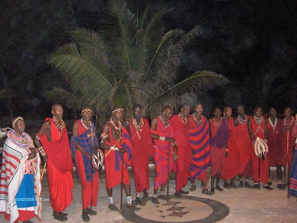 Maasai dancers in red robes at night, beaded necklaces under palms