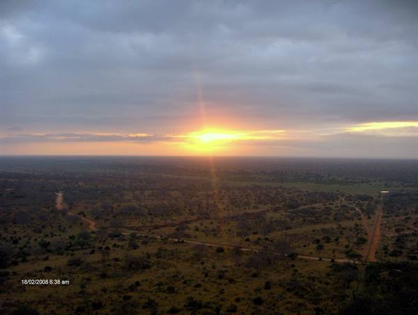 Sunrise over the savanna: sun breaking through grey clouds above bushes and dirt tracks