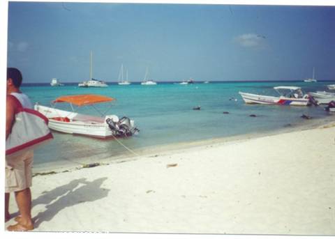 Small boats anchored by white beach, man with bag on the sand