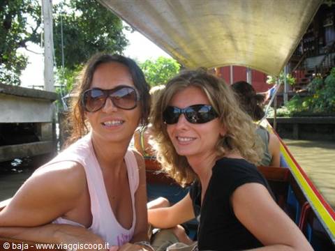 Two smiling women in sunglasses riding under a covered longtail boat on a canal
