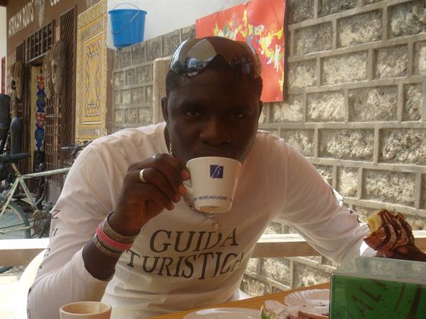 Man in Guida Turistica shirt sips coffee against stone wall