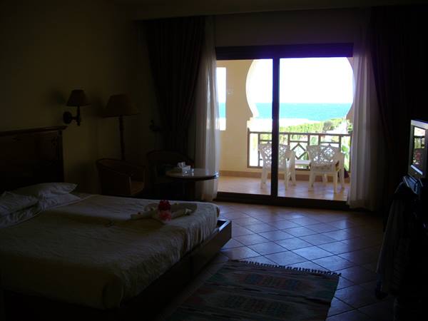 Dim hotel room, bed with towel swans, balcony overlooking the sea