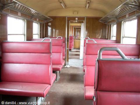 Empty train carriage with pink vinyl seats, wood panels and daylight from windows