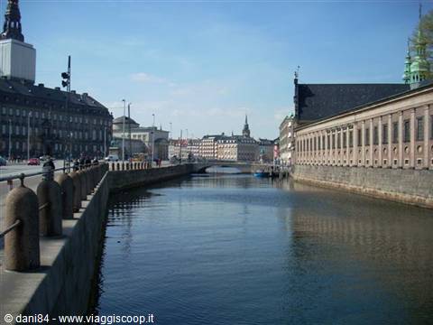 Urban canal in Copenhagen between historic buildings and a bridge under blue sky