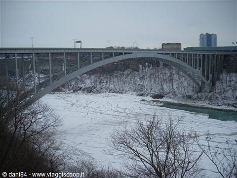 Arch bridge over frozen Niagara River, snowy banks under gray sky