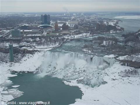 Frozen Niagara Falls in winter, water cascading between snow and city skyline