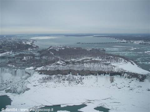 Frozen Niagara Falls, snow-covered island and icy river under grey sky