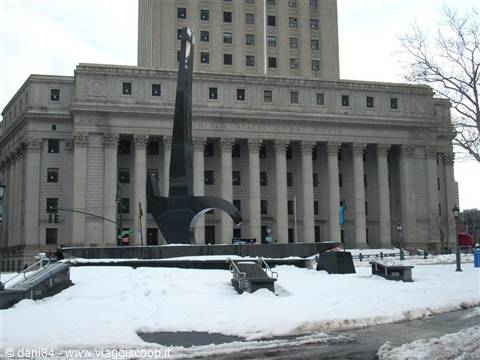 Black sculpture on snowy square in front of stone building with columns