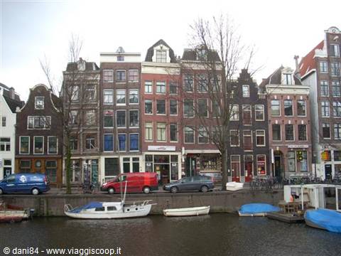 Amsterdam canal houses facade, cars and boats moored along the water