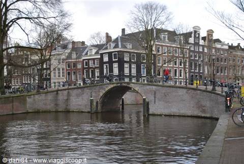 Brick bridge over Amsterdam canals, Dutch houses and bicycles under grey sky