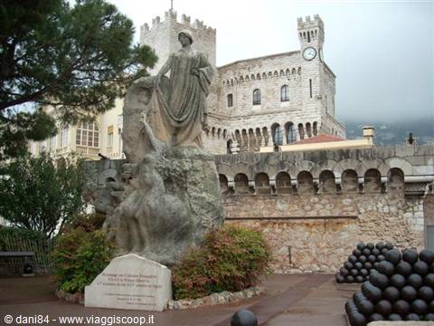 Stone statue in front of the Prince's Palace of Monaco, cannonball in foreground